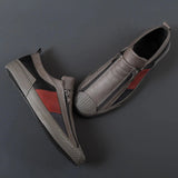 Men's grey slip-on sneakers with red accents, featuring a stylish and comfortable design, displayed on a vehicle hood with automotive elements in the background.
