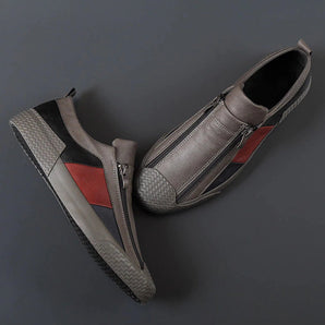 Men's grey slip-on sneakers with red accents, featuring a stylish and comfortable design, displayed on a vehicle hood with automotive elements in the background.