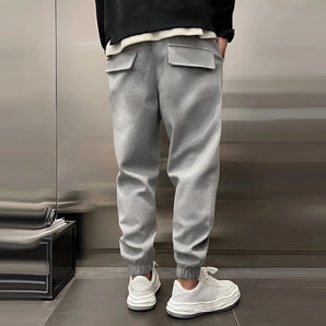 Men's grey tapered fleece joggers with zip pockets, focusing on the lower half of a person standing, showcasing the joggers' fitted design and comfortable fabric.