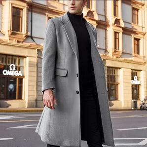 Men's grey wool winter coat displayed against a window backdrop, showcasing a stylish urban fashion design with a frock coat and trench coat influence. The overcoat features a sleek black neck detail and long sleeves, embodying a contemporary yet classic look in a size 3XL.