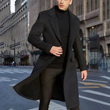 A man wearing a stylish urban fashion overcoat in grey wool, standing confidently. The coat features long sleeves and a structured shoulder design, epitomizing winter fashion. The individual is accessorized with sunglasses, enhancing the modern and sophisticated look.