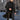 A man wearing a stylish urban fashion overcoat in grey wool, standing confidently. The coat features long sleeves and a structured shoulder design, epitomizing winter fashion. The individual is accessorized with sunglasses, enhancing the modern and sophisticated look.
