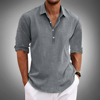 Men's lightweight blue linen shirt in a casual summer button-up style, featuring a classic collar and long sleeves, displayed on a model with a focus on the upper body. The shirt appears to have subtle grey tones, suitable for a relaxed yet polished look.