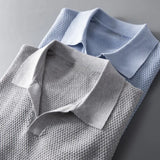 Men's luxury knit polo shirt in a stylish grey color with a classic collar and button design, featuring long sleeves and a breathable fabric. It is shown worn with an electric blue blazer, highlighting the shirt's designer and sophisticated look.