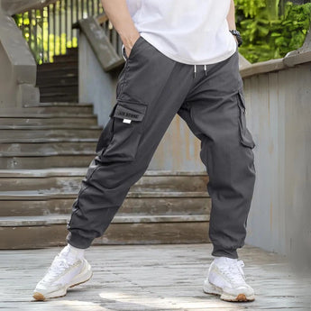Men wearing dark gray joggers in size 2XL, showing the pants' lightweight and water-resistant material, featuring zipper pockets.