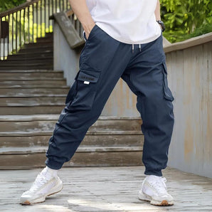 Men's navy blue joggers with lightweight, water-resistant fabric, featuring zipper pockets, shown being worn with focus on the waist, knee, and leg areas.