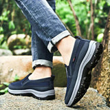 Men's navy waterproof slip-on walking shoes worn by a person standing on grass, showcasing the lightweight and anti-slip design.