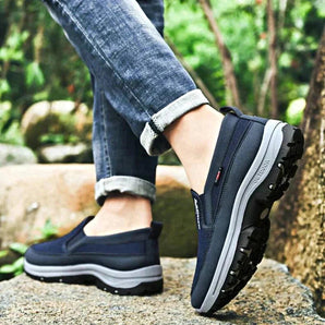 Men's navy waterproof slip-on walking shoes worn by a person standing on grass, showcasing the lightweight and anti-slip design.