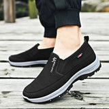 Men's navy waterproof slip-on walking shoes shown on a person's feet, highlighting the lightweight and anti-slip design. The shoes are styled with casual sportswear.