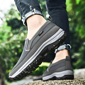 Men's navy waterproof slip-on walking shoes displayed on a person's feet, paired with jeans, showcasing their lightweight and anti-slip design in a natural outdoor setting.