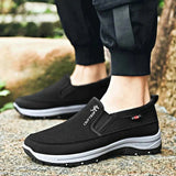 Men's navy slip-on walking shoes showcased outdoors, featuring a lightweight and waterproof design with anti-slip soles, paired with denim jeans on grass.