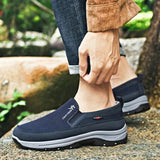 Men's navy waterproof slip-on walking shoes on a grass surface, featuring lightweight and anti-slip design, worn with denim pants.