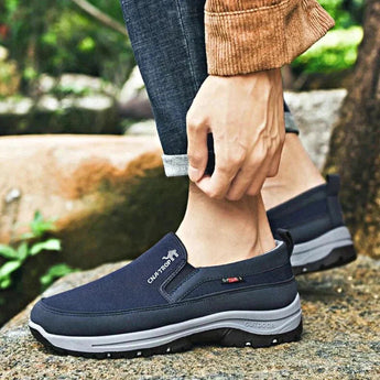 Men's navy waterproof slip-on walking shoes on a grass surface, featuring lightweight and anti-slip design, worn with denim pants.