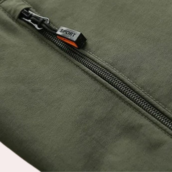 Men's olive green hooded cargo jacket with spacious front pockets, featuring long sleeves and a lightweight design ideal for urban wear. The jacket includes a windbreaker feature and a khaki-toned hue.