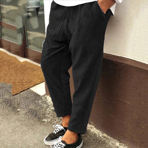 Men's slim fit black pleated trousers in a 5XL size, featuring a lightweight fabric suitable for urban fashion. The trousers are styled with a focus on modern tailoring, showcasing a sleek waistline and fitted thighs, ideal for a contemporary look.
