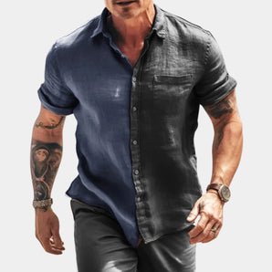 Men's slim-fit faded blue denim shirt with button-down design, featuring long sleeves, a collar, and a casual style. The shirt is worn by a person showing their arm and neck, and is paired with a black leather jacket.