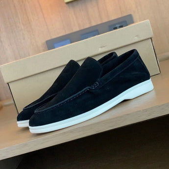 Men's tan suede loafers featuring comfortable slip-on design with contrast stitching, displayed on a hardwood floor.