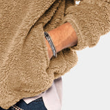Men's tan teddy bear hoodie made of faux fur with a zip-up front, featuring a fleece texture. The hoodie has long sleeves, a collar, and a cozy woolen appearance, modeled with jeans.