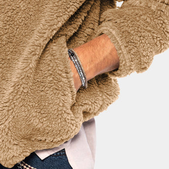 Men's tan teddy bear hoodie made of faux fur with a zip-up front, featuring a fleece texture. The hoodie has long sleeves, a collar, and a cozy woolen appearance, modeled with jeans.