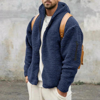 Men's tan teddy bear hoodie zip-up fleece jacket in faux fur, featuring long sleeves and a cozy collar. The model is wearing a marine blue variant in XL size, complementing the outerwear with a grey backdrop and beard, highlighting the garment's soft texture and stylish design.