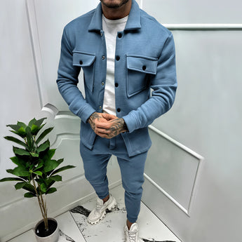 
A man standing indoors wearing a two-tone blue lightweight tracksuit, featuring long sleeves and a collar, in a stylish urban setting. He is possibly in a casual loungewear context, with a houseplant visible in the background. The tracksuit is labeled as "Azzurro" and is sized 3XL.