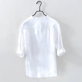Men's white linen shirt hanging on a clothes hanger, featuring a classic collar and long sleeves, designed for casual wear with a lightweight and breathable fabric.