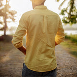 Men's yellow linen shirt with tailored fit, featuring a classic collar, button-down front, and long sleeves, displayed on a mannequin or model standing outdoors near plants and grass, highlighting the lightweight and breathable fabric.