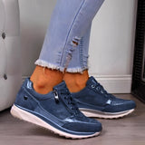 Metallic silver platform sneakers with blue accents displayed on a model wearing denim jeans. The sneakers are women's trendy footwear, size 43, positioned outdoors with a hint of greenery in the background, highlighting their sporty and stylish design.