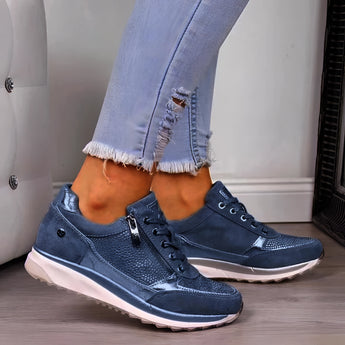 Metallic silver platform sneakers with blue accents displayed on a model wearing denim jeans. The sneakers are women's trendy footwear, size 43, positioned outdoors with a hint of greenery in the background, highlighting their sporty and stylish design.