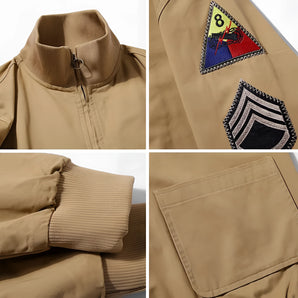 Military style khaki bomber jacket featuring embroidered patches on the sleeves and chest, with a ribbed collar and cuffs.