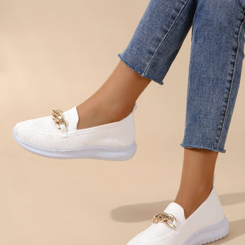 A minimalist white sneaker with a seamless design and lightweight sole, shown on a person wearing grey jeans against a light azure background, highlighting modern fashion and style.