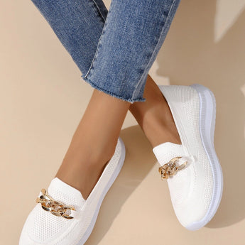 Minimalist white sneaker featuring a seamless design and lightweight sole, worn on a human leg in a fashion-forward setting, with the person dressed in a stylish electric blue blazer.