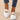 Minimalist white sneaker with a seamless design and lightweight sole, worn on a human leg, showcasing the shoe's sleek and modern appearance.