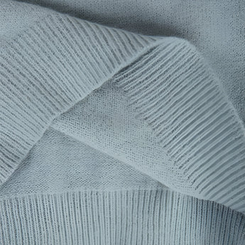 Mint green Fair Isle women's sweater with a cozy Scandinavian knit pattern, featuring intricate geometric designs in shades of grey and electric blue. The sweater is displayed against a wooden backdrop, highlighting the textile's texture and pattern.