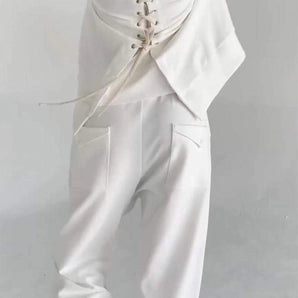 Modern white blouse with lace-up design paired with high-waist designer pants, featuring long sleeves and a tailored fit on a model.