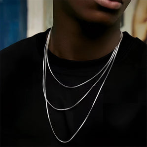 A woman wearing a multi-layer minimalist silver necklace around her neck, with focus on her shoulders and upper chest.