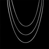 A multi-layer minimalist silver necklace with crescent and circular pendants, shown in a dark background.
