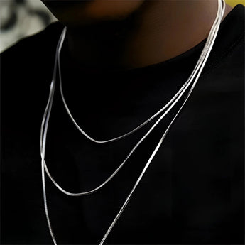 A woman wearing a multi-layer minimalist silver necklace, showcasing its lightweight and versatile design against a grey top, focusing on the neck and chest area.