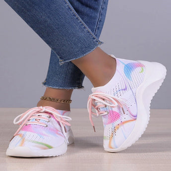 A pair of multicolor women's breathable lightweight athletic sneakers with a design featuring shades of grey, pink, and aqua, worn on a person standing against a white background.