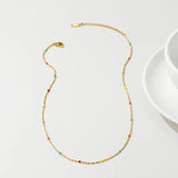 A multicolored gemstone necklace with gold beads displayed on a white background.