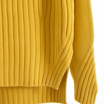 Mustard yellow pleated turtleneck sweater displayed on a wooden surface.