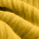 A mustard yellow pleated turtleneck sweater, perfect for cozy winter wear, displayed on a wooden background with leaf and grass elements to complement the warm knit texture.