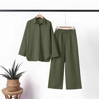 Navy blue linen summer suit displayed on a clothes hanger, featuring a short-sleeved top and matching pants, designed for mature women. The suit is set against a neutral background with a subtle presence of houseplants in flowerpots contributing to a casual, natural ambiance.