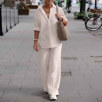 
A mature woman wearing a navy blue linen summer suit with a dress shirt and standing outdoors near a bicycle.