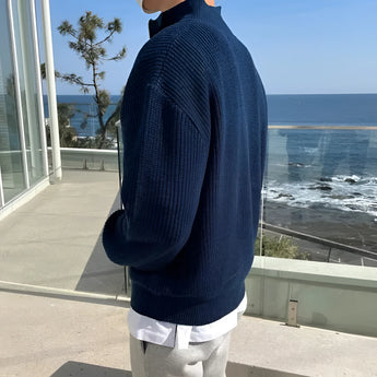 
A man wearing a navy blue ribbed zip-up sweater, suitable for cozy fall fashion, paired with jeans and standing outdoors.