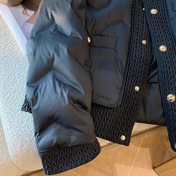 
A navy blue quilted designer puffer jacket with a high collar, designed for winter wear, displayed on a wooden floor. The jacket features long sleeves and a stylish, comfortable fit.