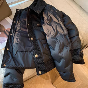 Navy blue quilted puffer jacket with a high collar, featuring long sleeves and a sleek design suitable for winter wear. The jacket is displayed against a wooden floor background.
