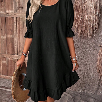 Woman wearing a black ruffle dress with a round neck, short sleeves, and fitted waist, standing upright.