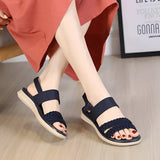 Navy blue women's comfort sandals with a braided strap design, shown on a model wearing a red dress.