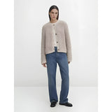 A woman wearing a navy bouclé jacket over a dress shirt, featuring a chunky knit texture. The jacket includes a collar, long sleeves, and resembles a blazer style, suitable for winter wear. The outfit is complemented by jeans, creating a casual yet polished look.